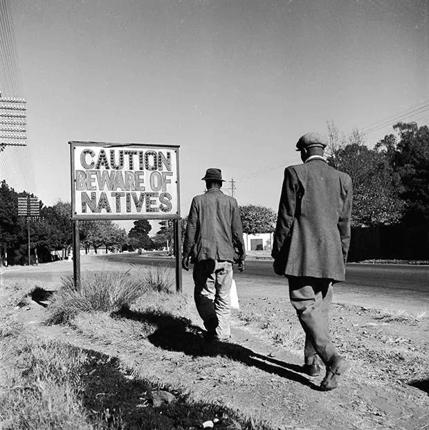 Dos africanos pasan junto a un letrero común en el apartheid de Sudáfrica, Johannesburgo. (1956)