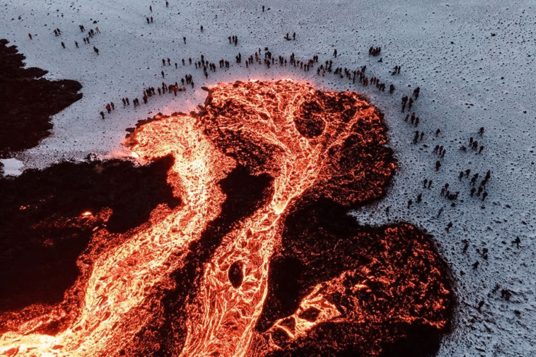 Lava que fluye en la nieve en Islandia mientras una multitud de personas toma el sol cerca de ella mientras observa.