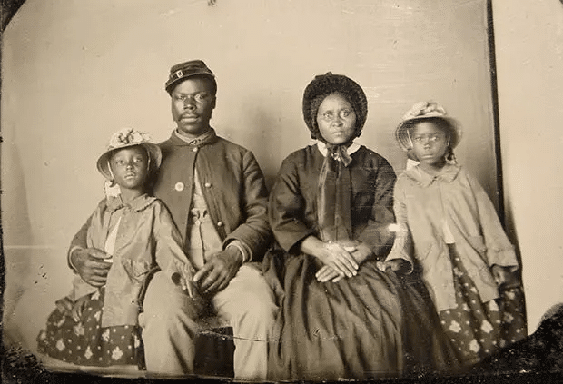 Fotografía que muestra al soldado en uniforme, la esposa con vestido y sombrero, y dos hijas con abrigos y sombreros a juego.