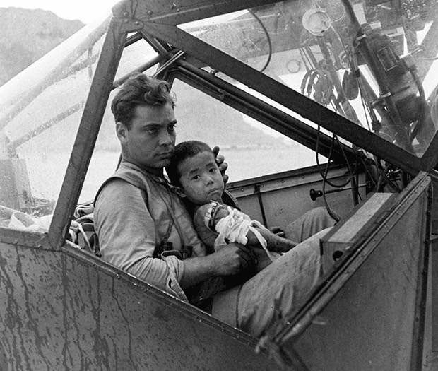 Un soldado estadounidense acuna a un niño japonés herido y lo protege de la lluvia en la cabina de un avión durante la Batalla de Saipan mientras espera para transportarlo a un hospital de campaña en julio de 1944. Fotografía de Peter Stackpole.