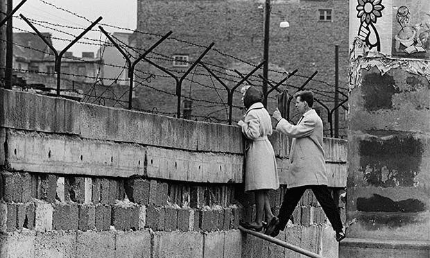 Una mujer joven, acompañada de su novio, se encuentra de pie en un lugar precario cerca de la parte superior del Muro de Berlín para hablar con su madre en el lado de Berlín Este. 21 de abril de 1962.